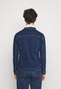 Temno moderna denim jakna s krznim ovratnikom, ozek kroj, vidno šivanje ter gumbi na manžetah in robu.