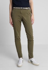 Olivgrön chinos med slim fit, sidofickor och ett vävt svart och vitt bälte. I hop med vita sneakers.