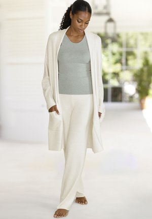 Hellcremefarbenes Lounge-Set bestehend aus einer langen Strickjacke mit Taschen und locker sitzenden Hosen, kombiniert mit einem hellgrauen, enganliegenden Tanktop.