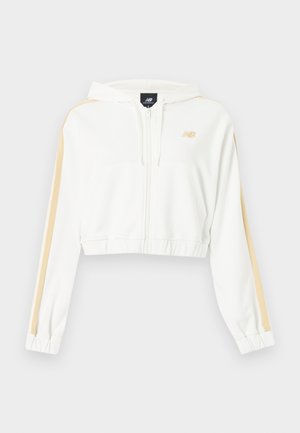 Weißer, kurz geschnittener Kapuzenpullover mit Reißverschluss, beigen Streifen an den Ärmeln, elastischen Bündchen und Saum sowie kleinem New Balance-Logo auf der Brust.