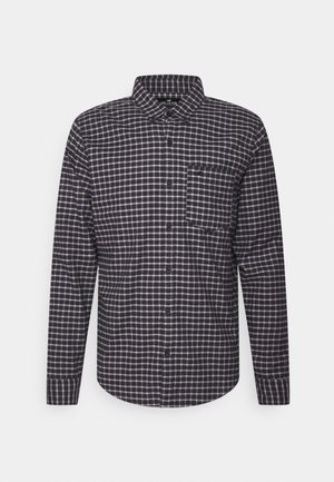 Chemise à manches longues à carreaux noir et blanc, boutonnée, avec col et poche poitrine, présentée sur un fond uni.