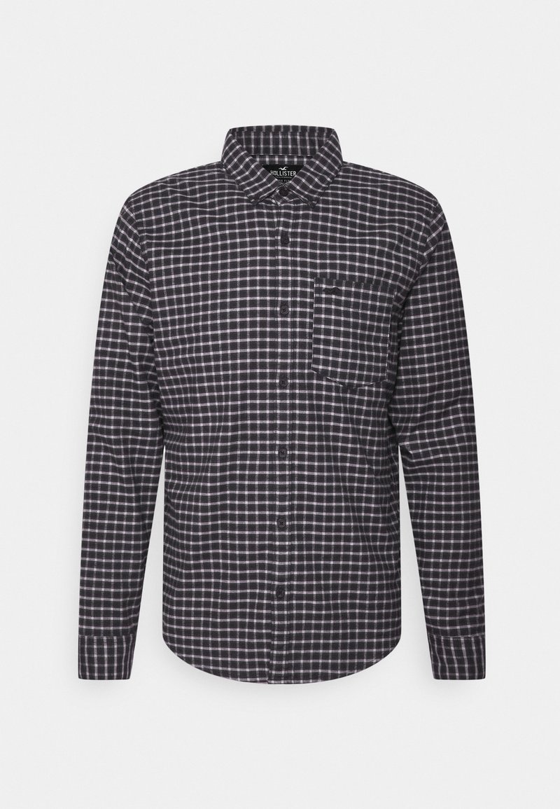 Chemise à manches longues à carreaux noir et blanc, boutonnée, avec col et poche poitrine, présentée sur un fond uni.