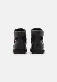 Botas negras de media caña, hechas de cuero y ante, con un collarín acolchado, lados texturizados y un acento de logo rojo en el talón.