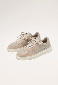 Zapatillas beige con una combinación de cuero liso y ante. Punta redondeada, cuello acolchado y cordones clásicos. Suela de goma blanca con detalles perforados.