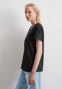 Zwarte V-hals T-shirt met korte mouwen, gemaakt van zachte stof. Heeft een relaxte fit en een soepele textuur, gecombineerd met lichtblauwe jeans.