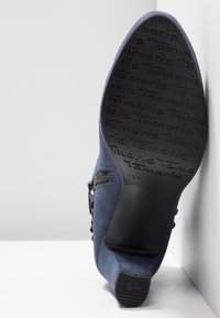 Bottine femme bleu marine inclinée vers le haut pour afficher la semelle avec un motif de texte répétitif "tamaris" et une indication de taille 37.