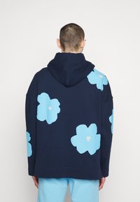 Felpa con cappuccio blu navy dal taglio morbido, con grandi motivi floreali azzurri e dettagli color crema sul retro. Tessuto morbido e strutturato.