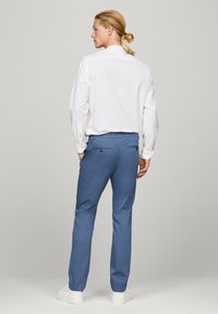 Pantaloni azzurri chiari realizzati in un tessuto morbido, con un taglio classico, tasche posteriori con chiusure a bottone, abbinati a una camicia bianca.