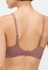 BH i mauve med justerbare stropper, glatt tekstur, krok-og-løkke lukking, og subtilt krone-logo på baksiden.