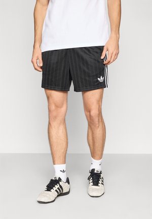 Czarne sportowe spodenki z pionowym, teksturowanym wzorem pasków, białe logo Adidas, do tego biała koszulka, czarno-białe sportowe buty oraz skarpetki.