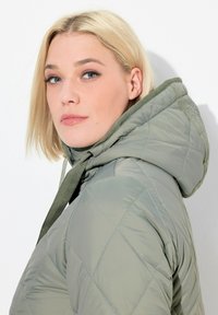 Gequilted pufferjack in lichtgroen met een gestructureerde afwerking en capuchon. Kenmerkt zich door diagonale stiksels en verstelbare trekkoorden.