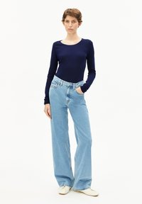 Marinebluse mit langen Ärmeln, hellblaue weit geschnittene Jeans, cremefarbene Schuhe; glatte Textur, einfaches Design, mit klassischem Schnitt.