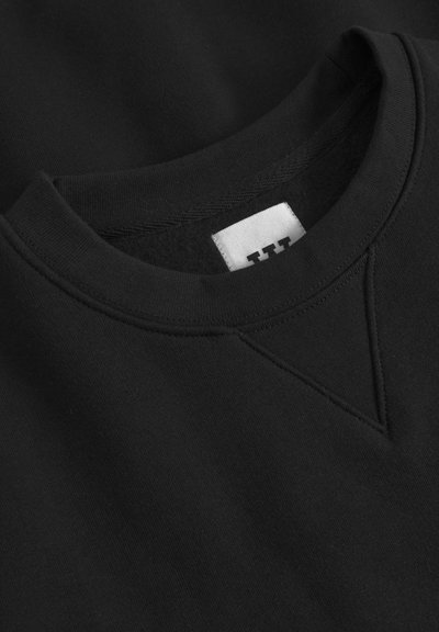 Schwarzer Pullover mit Rundhalsausschnitt und V-Nähdetail am Kragen. Hergestellt aus weichem Stoff mit glatter Textur. Weißes Etikett innen.