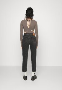 Brun långärmad topp med en utskärning på ryggen, parat med svarta högmidjade jeans och svarta skor. Vita strumpor synliga.