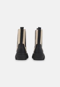 Juodos ir smėlinės spalvos aulinukai iki kulkšnių su storesniu padu, elastinėmis šoninėmis juostomis ir užsegimu gale; lygios odos ir textured akcentai.