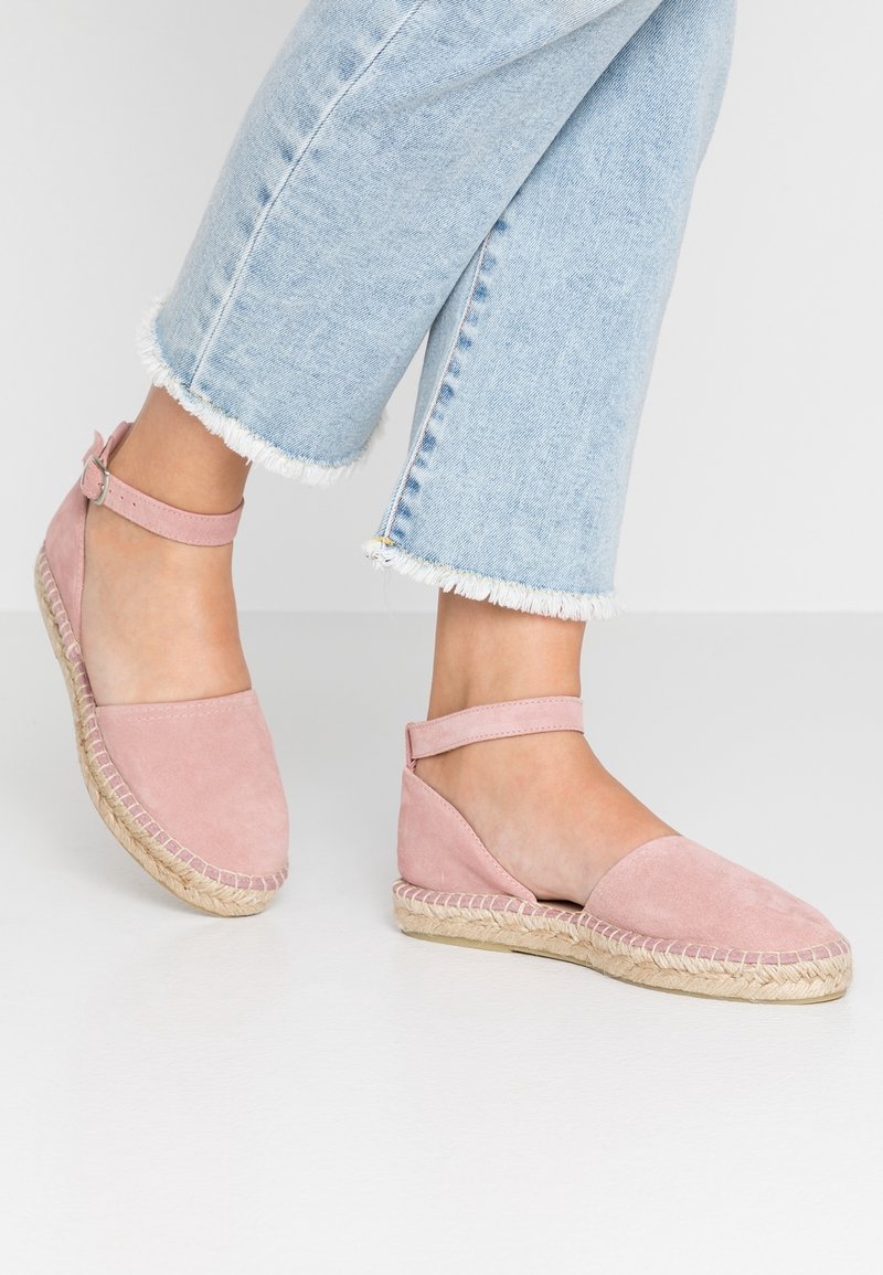 Różowe zamszowe espadryle z paskiem na kostkę, okrągłym noskiem i plecioną platformą z juty. Posiadają płaską podeszwę i przetarte dżinsowe spodnie.