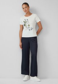 Witte T-shirt met een grafisch ontwerp in groen en zwart, gecombineerd met marineblauwe brede broek en witte sneakers. Soepele stof textuur.