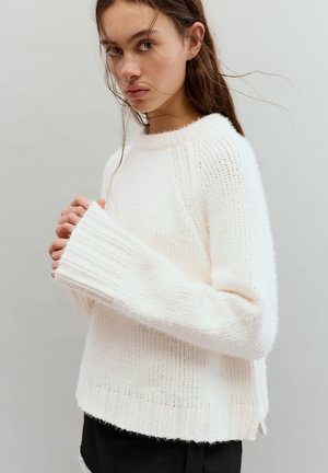 Pulover crem din tricot cu tiv și manșete rib, cu un design lejer și textură moale. Fante laterale jos evidențiază forma.