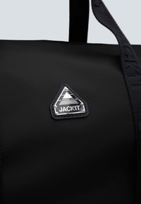 Borsa duffel nera con finitura testurizzata, caratterizzata da un patch logo triangolare con "JACK1T" in argento e una tracolla resistente.