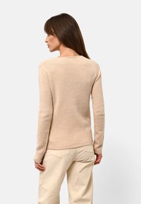 Beige gestrickter Pullover mit rundem Ausschnitt und langen Ärmeln. Glatte Textur, taillierte Passform und dezente Rippdetails an den Bündchen und dem Saum.