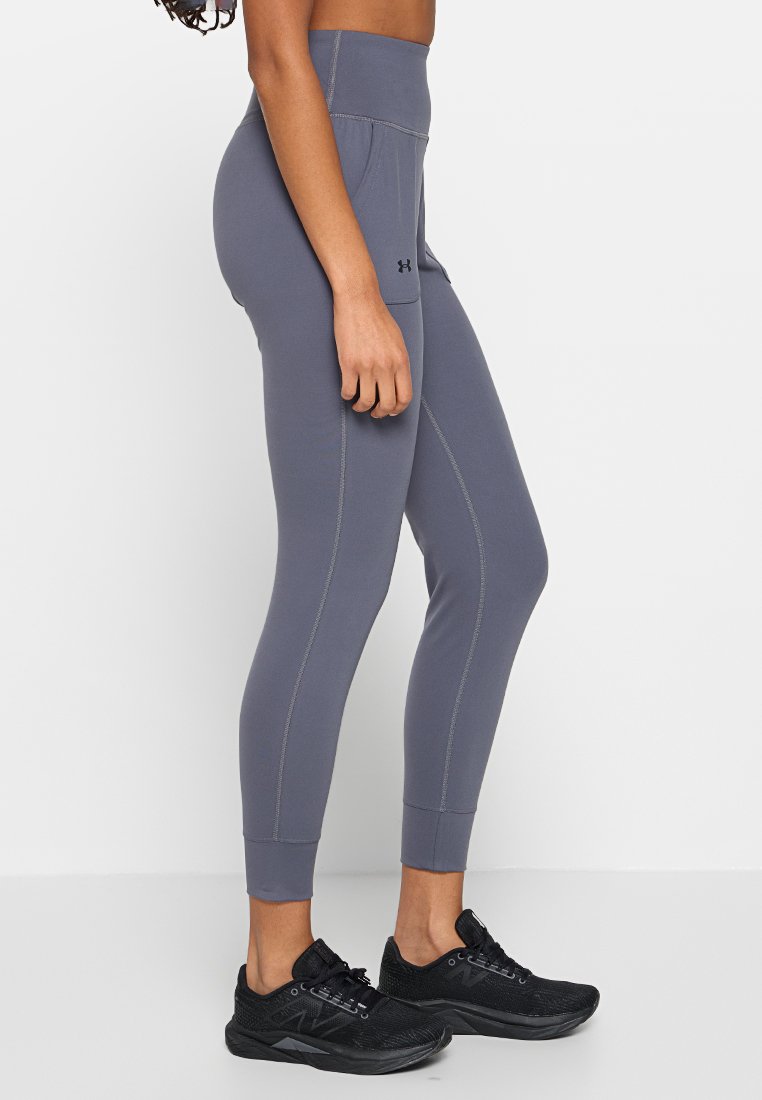 Leggings de sport gris avec une taille haute, présentant des coutures plates et une poche latérale, associés à des chaussures de course noires.