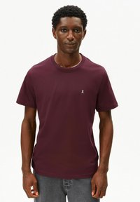 Bordeauxrode katoenen T-shirt met ronde hals en korte mouwen, met een klein lichtkleurig lintembleem op de linkerborst.