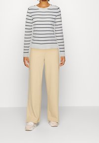 Randig långärmad tröja i ljusblått och marinblått, matchad med beige vida byxor och ljusrosa sneakers, med knappar som detalj på tröjan.