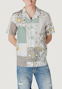 Camisa de manga corta, abotonada, con un diseño de patchwork en tonos de verde, gris y blanco, que presenta patrones florales y geométricos.
