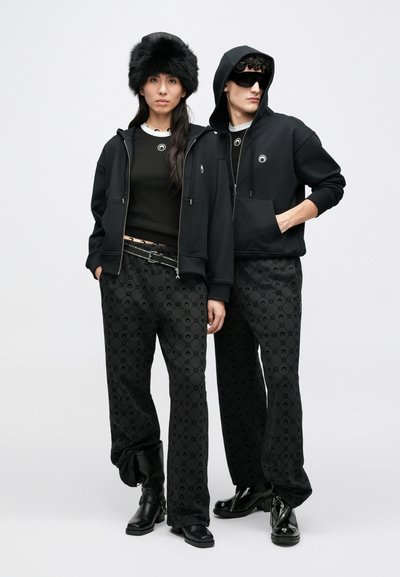 Sweatshirts pretas com capuz combinadas com calças pretas estampadas apresentam um logótipo subtil, complementadas por um chapéu de pêlo e botas pretas brilhantes.