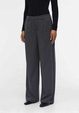 Mannequin portant un pantalon gris foncé taille haute à jambes larges avec poches latérales, associé à un haut noir à manches longues et des chaussures pointues noires.