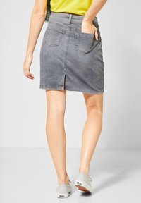 Grå denimkjol med medellång längd vid låren, bakfickor och en liten slits vid fållen. Stylad med avslappnade skor och en ljus topp.