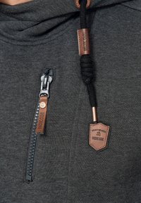 Sudadera gris oscura con una textura suave; presenta un cierre de cremallera diagonal, etiquetas de acento de cuero y un capucho con cordón anudado.
