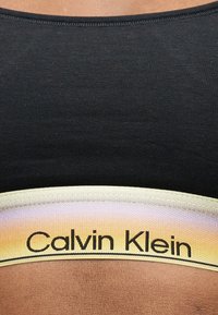 Κοντινή λήψη μαύρου υφάσματος με μπεζ ελαστική ταινία με την επιγραφή «Calvin Klein» στην κάτω άκρη.