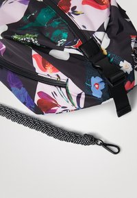 Sac à dos floral multicolore en tissu brillant et imperméable ; il possède une fermeture éclair noire, une sangle réglable et un accessoire noir texturé.