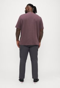Kurzärmliges, muted lila Baumwoll-T-Shirt mit rundem Ausschnitt, kombiniert mit dunkelgrauen Cargo-Hosen mit Seitentaschen und einer lockeren Passform.