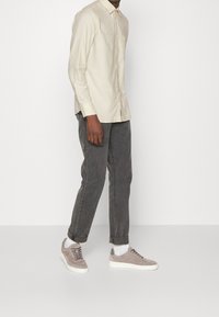 Lichtbeige overhemd met lange mouwen en een button-down kraag, grijze relaxte broek en lichtgrijze suède sneakers met witte zolen.