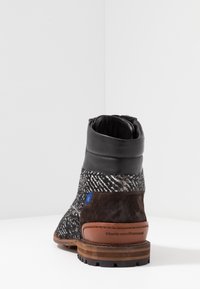 Bottine noire et marron avec tissu texturé, cuir au niveau de la cheville, semelle en bois empilée et détail de talon marqué.