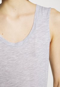 Šviesiai pilkas liemenėlė su apvaliu iškirpimu, pagaminta iš minkštos, tekstūruotos medžiagos. Turi laisvą kirpimą ir subtilų meluotą raštą.