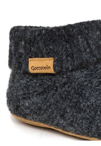 Pantofole grigie in feltro con superficie testurizzata, dotate di un'etichetta in pelle marrone con la scritta "Gottstein" sul lato e una suola in gomma beige.
