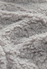 Gros plan sur un tissu polaire doux, gris et texturé avec des boucles visibles et une surface douillette et pelucheuse.
