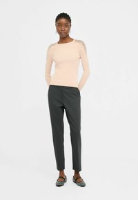 Maglietta a maniche lunghe rosa chiaro a coste con dettagli testurizzati sulle spalle, abbinata a pantaloni tapered grigio scuro e scarpe flat nere.