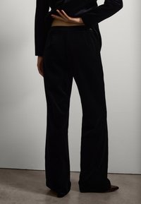 Schwarze Samt-Hosen mit weitem Bein und glatter Textur, die eine maßgeschneiderte Passform und einen leichten Schlag am Saum aufweisen, getragen mit einem figurbetonten Oberteil.