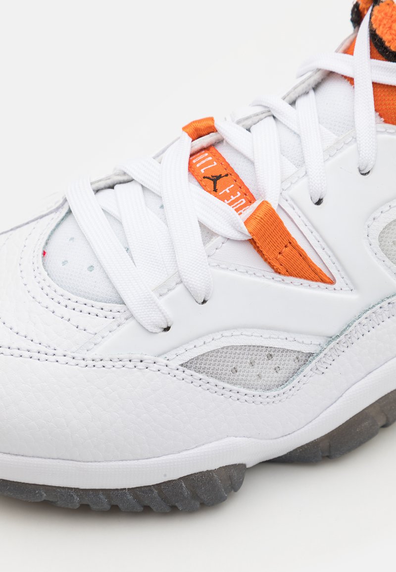 Sneaker bianca e arancione con lacci bianchi, pannelli in rete, pelle testurizzata e cuciture visibili su uno sfondo chiaro.