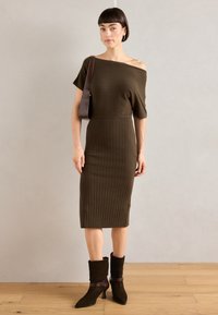 Brown ribbed knit dress with an off-the-shoulder design. Styled with brown suede ankle boots and a brown shoulder bag. Simple texture.