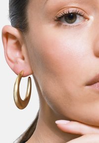 Kullanımı rahat altın halka küpe, pürüzsüz ve kavisli bir şekle sahiptir. Hafif tasarımı açık bir bölüm içerir ve minimalist görünümü vurgular.