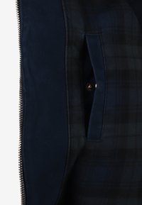 Granatowa kurtka zapinana na zamek, z miękkim wykładem w kratkę, boczną kieszenią i metalowym zatrzaskiem, zapewniającym pewne zapięcie.