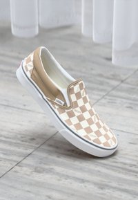 Bež i bijeli karirani slip-on Vans tenisice s bijelim gumeni potplat i malim crvenim naglaskom na peti. Glatka tekstura tkanine.