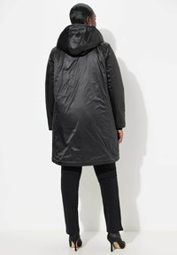 Cappotto nero con cappuccio, dal finish liscio e lucido. La lunghezza arriva a metà coscia, con maniche lunghe e taglio dritto.