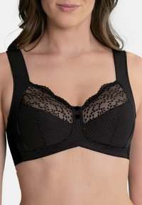Schwarzer BH mit gepunktetem Muster, transparenter Spitzenoberteil mit floralem Design und dicken Trägern mit gewellten Kanten sowie zwei Knöpfen in der Mitte.