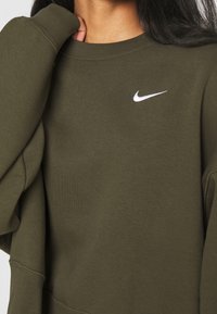 Olive green sweatshirt made of soft fabric, featuring a round neck and long sleeves, with a white Nike logo on the upper left chest.
